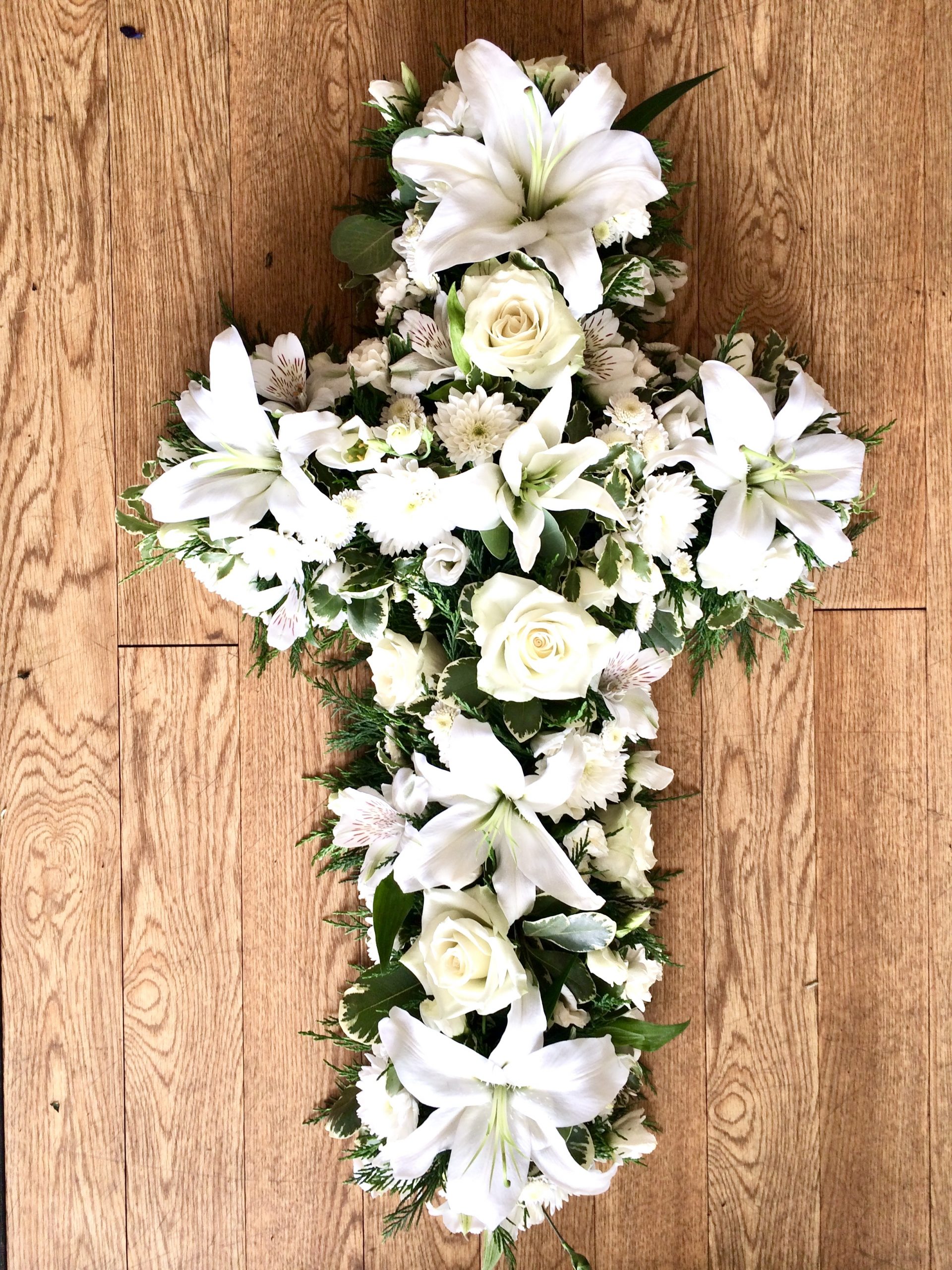 An elegant open cross tribute in all white with lush foliage. Flower colour of your choice. 24 hours notice. Due to seasonal variations some items may be substituted to produce a display of equal quality and value. Professionally arranged by our expert florists with care. Delivered by hand by our own driver. Click & collect is also available